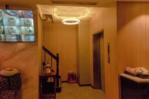 A hotel hallway with a wooden floor, a staircase, a reception desk, and a television screen displaying multiple rooms. - Newful Hotel (Taipei)
