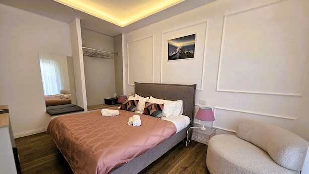 A hotel room with a bed, bedside table, lamp, chair, and a picture on the wall. - Riviera Suites Stanza 1 - by Be Your Home (Civitavecchia)