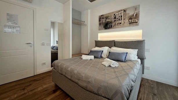 Une chambre à coucher avec un grand lit, une tête de lit dotée d’un éclairage intégré, un miroir et une œuvre d’art accrochée au mur.