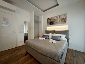 A bedroom with a large bed, a headboard with integrated lighting, a mirror, and a wall-mounted artwork. - Riviera Suites Stanza 2 - by Be Your Home (Civitavecchia)