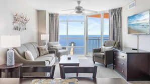 A spacious living room with a large window offering a view of the ocean and pier, a ceiling fan, and a flat-screen TV mounted on the wall. - Prince Resort Oceanfront 3BR Pools Lazy River (north myrtle beach)