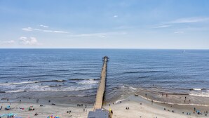 A pier extending into the ocean with beachgoers and beach umbrellas. - Prince Resort Oceanfront 3BR Pools Lazy River (north myrtle beach)
