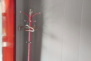 A room with a red door, a grey wall, and a pink coat rack with several hangers. - Quanjiao Jin'an Business Hotel (Quanjiao)