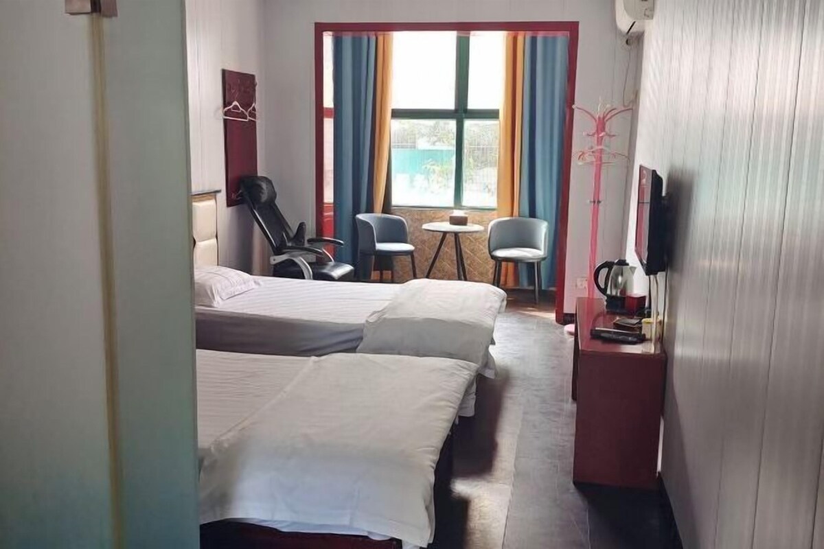 A hotel room with two beds, a small table, two chairs, a TV, and a window with curtains.
