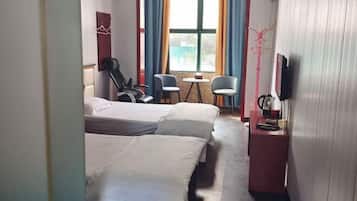 A hotel room with two beds, a small table, two chairs, a TV, and a window with curtains.
