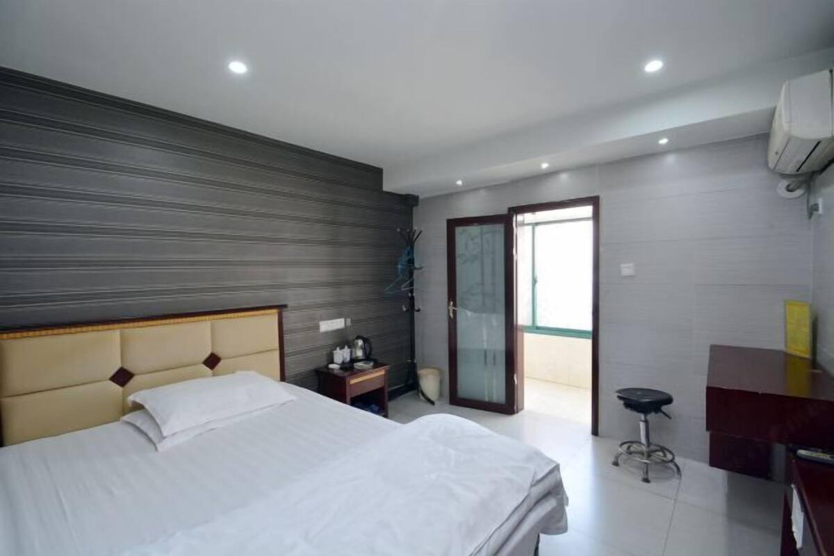 A modern hotel room with a bed, a desk, a chair, and a sliding glass door leading to a balcony.