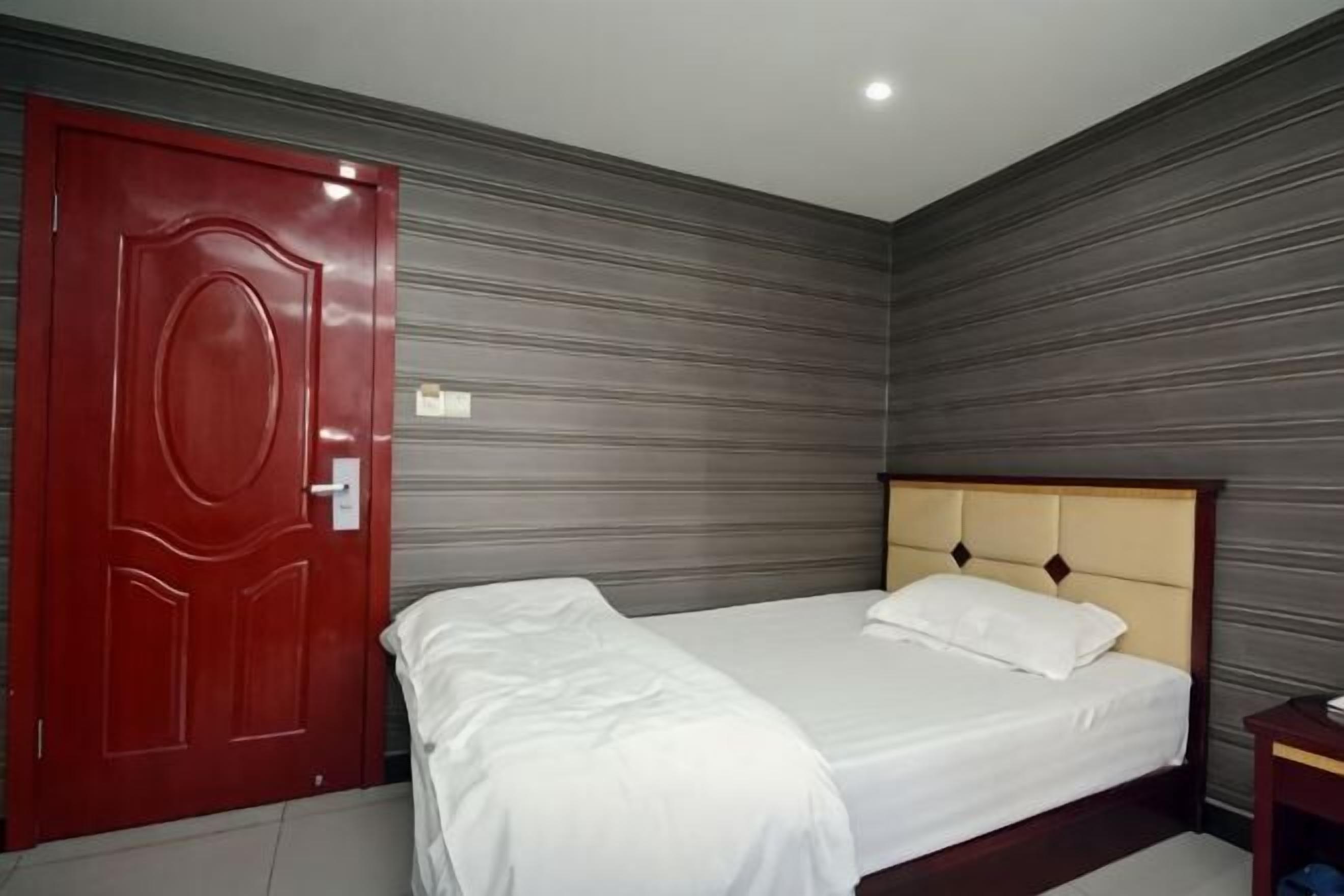 A room with a bed, a red door, and a grey wall.