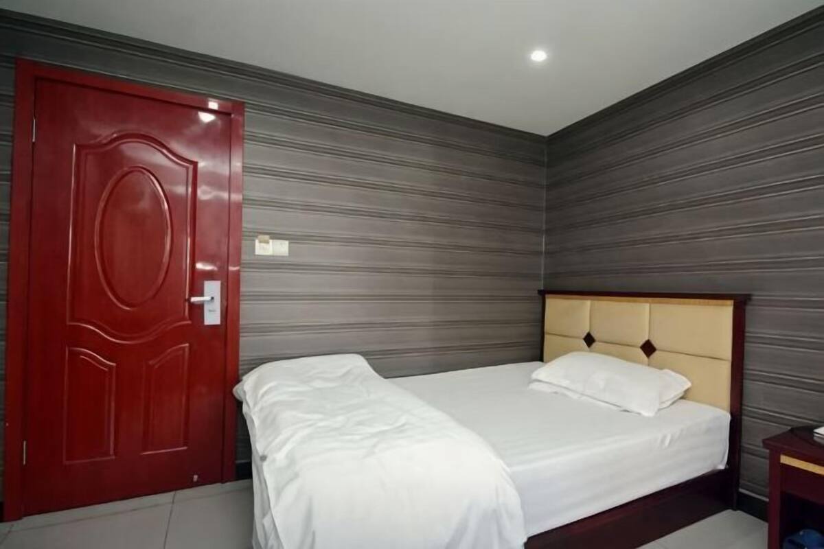 A room with a bed, a red door, and a grey wall.