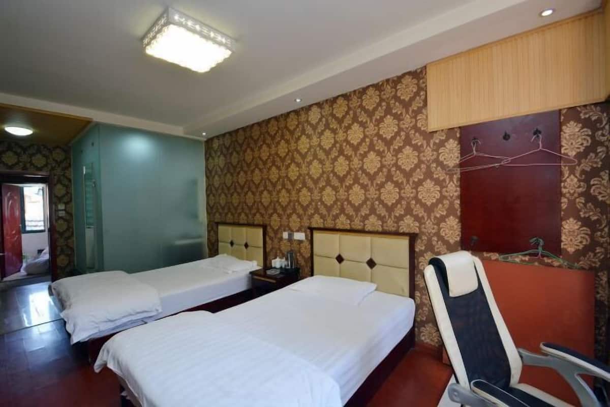 A hotel room with two beds, a chair, a wardrobe, and a mirror.