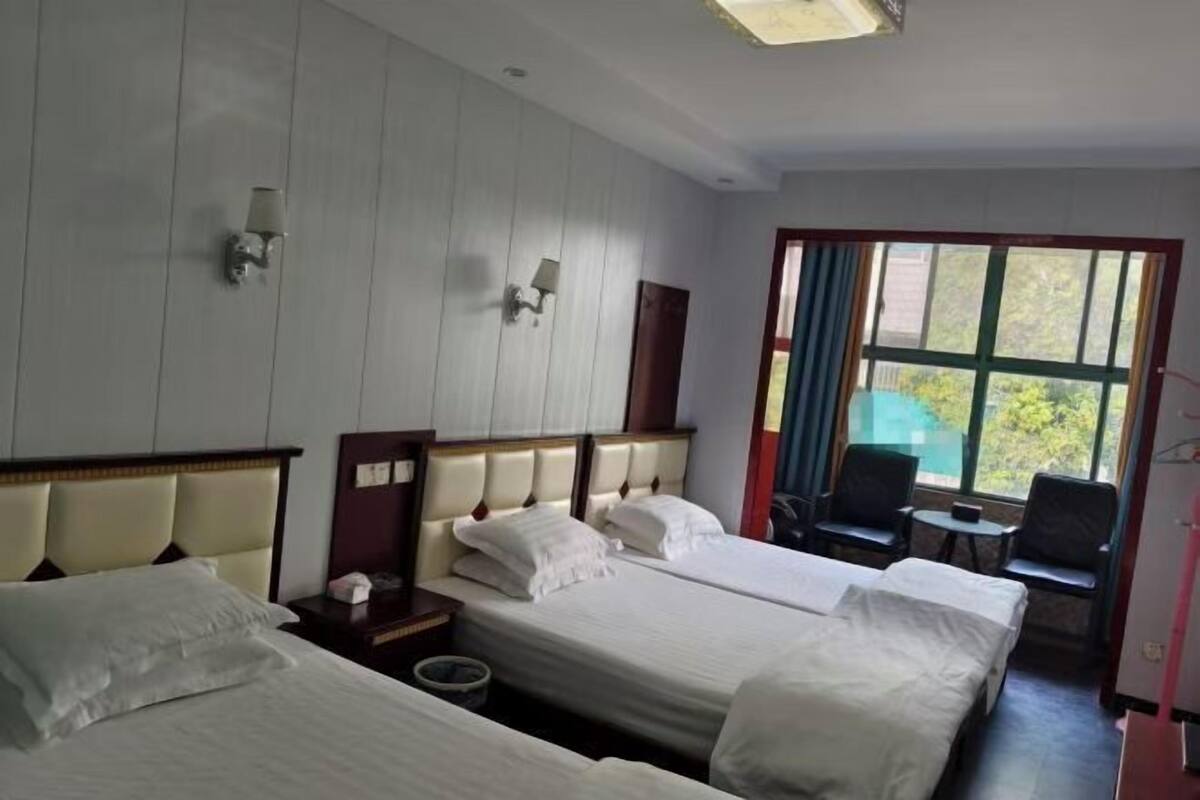 A hotel room with two beds, a small table, a chair, and a window with curtains.
