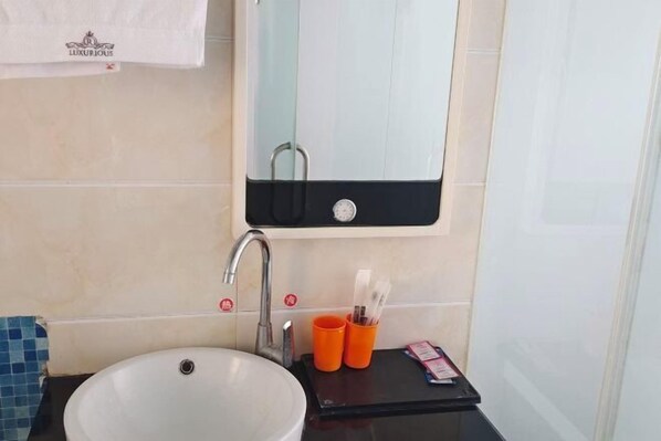A bathroom with a white sink, a mirror above it, and a black countertop with orange cups and a tissue box. - Quanjiao Jin'an Business Hotel (Quanjiao)