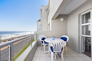 Enjoy the ocean view from this balcony with a table and chairs.