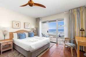 A hotel room with a bed, a desk, a chair, a ceiling fan, and a view of the ocean. - Sea Spray A410 - Studio Apartment, Sleeps 2 (Cape Town)