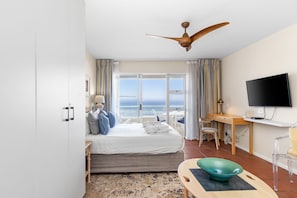 Una habitación de hotel con cama, escritorio, televisor y vista al océano.