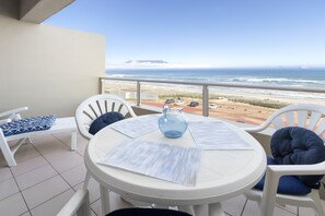 Balcón con mesa y sillas, con vista a una playa y al océano.