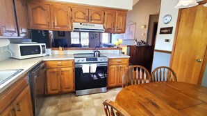 A compact kitchen with wooden cabinets, a microwave, a stove, and a dining table with chairs. - THREE BEDROOM,THREE BATH CONDO WITH HUGE DECK LOCATED ON THE ISLAND! (Holiday Island)