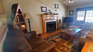 A living room with a fireplace, a sofa, a coffee table, and a television. - THREE BEDROOM,THREE BATH CONDO WITH HUGE DECK LOCATED ON THE ISLAND! (Holiday Island)