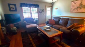 A living room with a sofa, a coffee table, a TV, and a window with blinds. - THREE BEDROOM,THREE BATH CONDO WITH HUGE DECK LOCATED ON THE ISLAND! (Holiday Island)