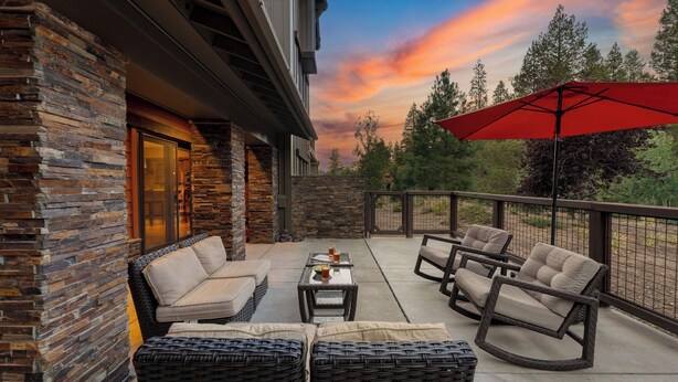 A patio with wicker furniture, a red umbrella, and a stone wall. - Luxe All-season Retreat by Avantstay Prime Location, Near Skiing (Truckee)