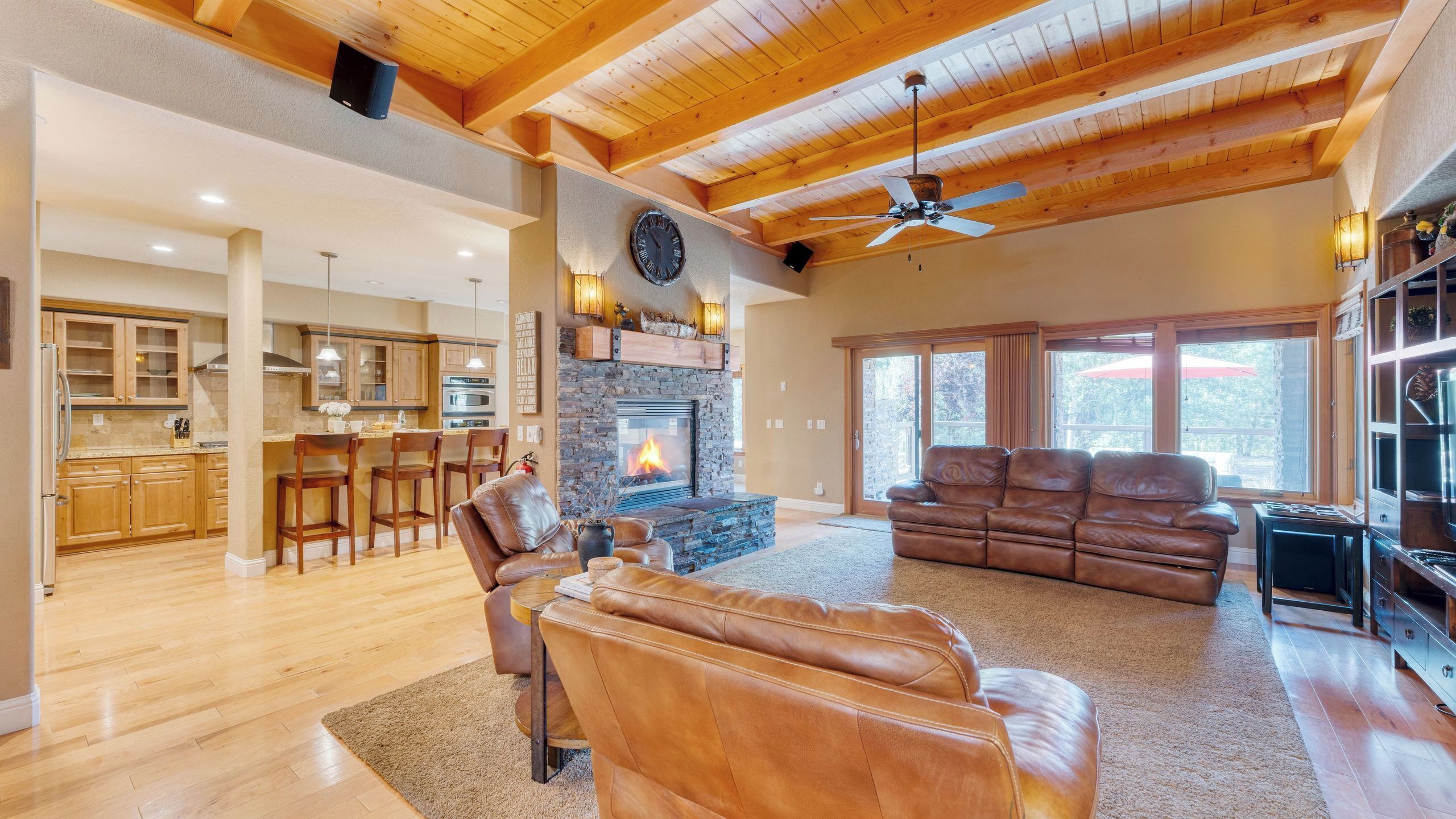 A spacious living area with a fireplace, leather sofa, and a dining area with wooden cabinets and bar stools.