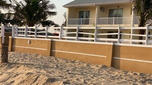 Una propiedad frente a la playa con un edificio de dos pisos, una cerca blanca y una playa de arena.