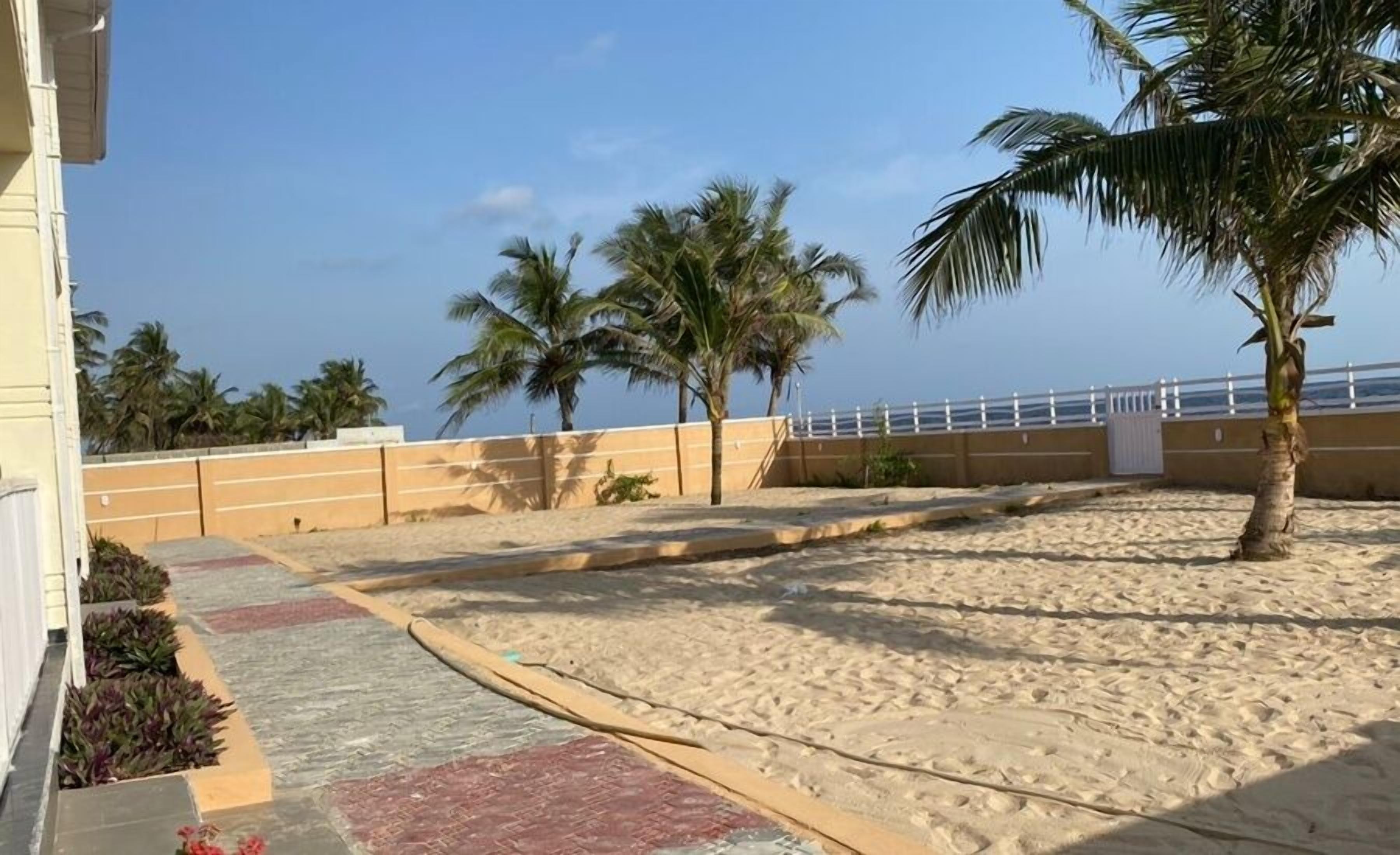 A sandy beach area with palm trees and a white fence.