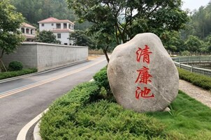 Piedra con texto rojo en un área ajardinada al lado de una carretera.