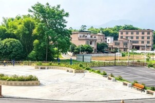 Un estacionamiento con un banco, rodeado de vegetación y edificios al fondo.