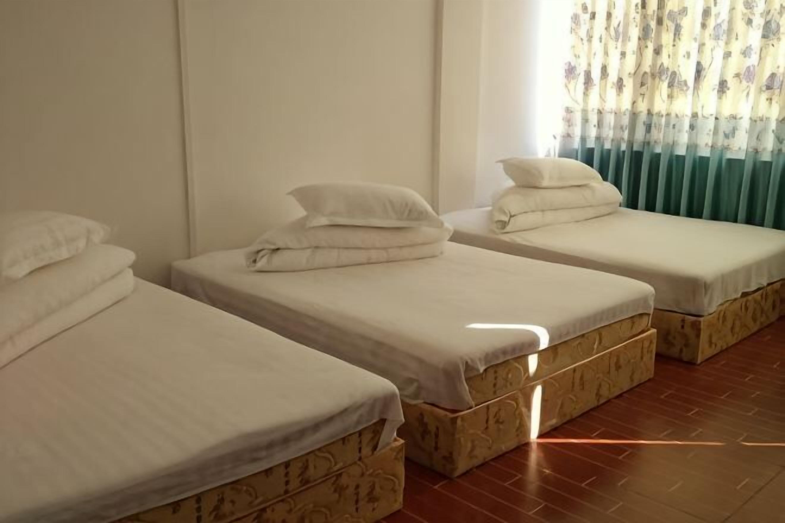 A room with three single beds, each with a mattress and pillow, and a window with curtains.