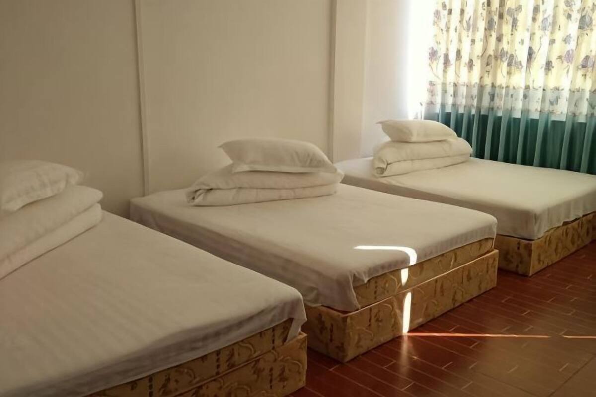 A room with three single beds, each with a mattress and pillow, and a window with curtains.