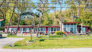 Un bâtiment rouge doté de grandes fenêtres, une allée gravillonnée et un espace clos planté d’arbres.