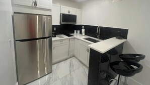 A modern kitchen with white cabinets, a stainless steel refrigerator, a black microwave, and a black backsplash. - Chic 1-bedroom apartment with AC, WiFi in fantastic Fort Myers (Fort Myers)