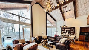 A spacious living room with a large fireplace, wooden flooring, and a view of the outdoors through large windows. - Charming 4-bedroom Ski house in Stratton with Shuttle or walk to slope. (Stratton)