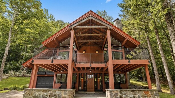 A two-story log cabin with a balcony on the upper level, surrounded by trees. - Charming 4-bedroom Ski house in Stratton with Shuttle or walk to slope. (Stratton)