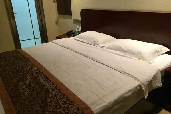 Habitación de hotel con una cama grande, cabecero de madera, mesita de noche con teléfono y alfombra estampada.