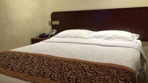 Una cama bien tendida con una colcha estampada, un cabecero de madera y una mesita de noche con un teléfono.