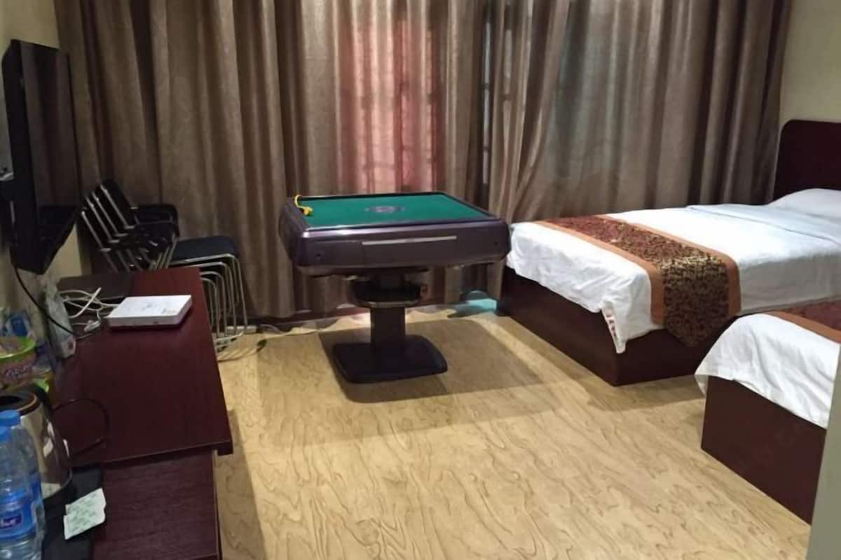 A hotel room with a pool table, two beds, a desk with a chair, and a TV.