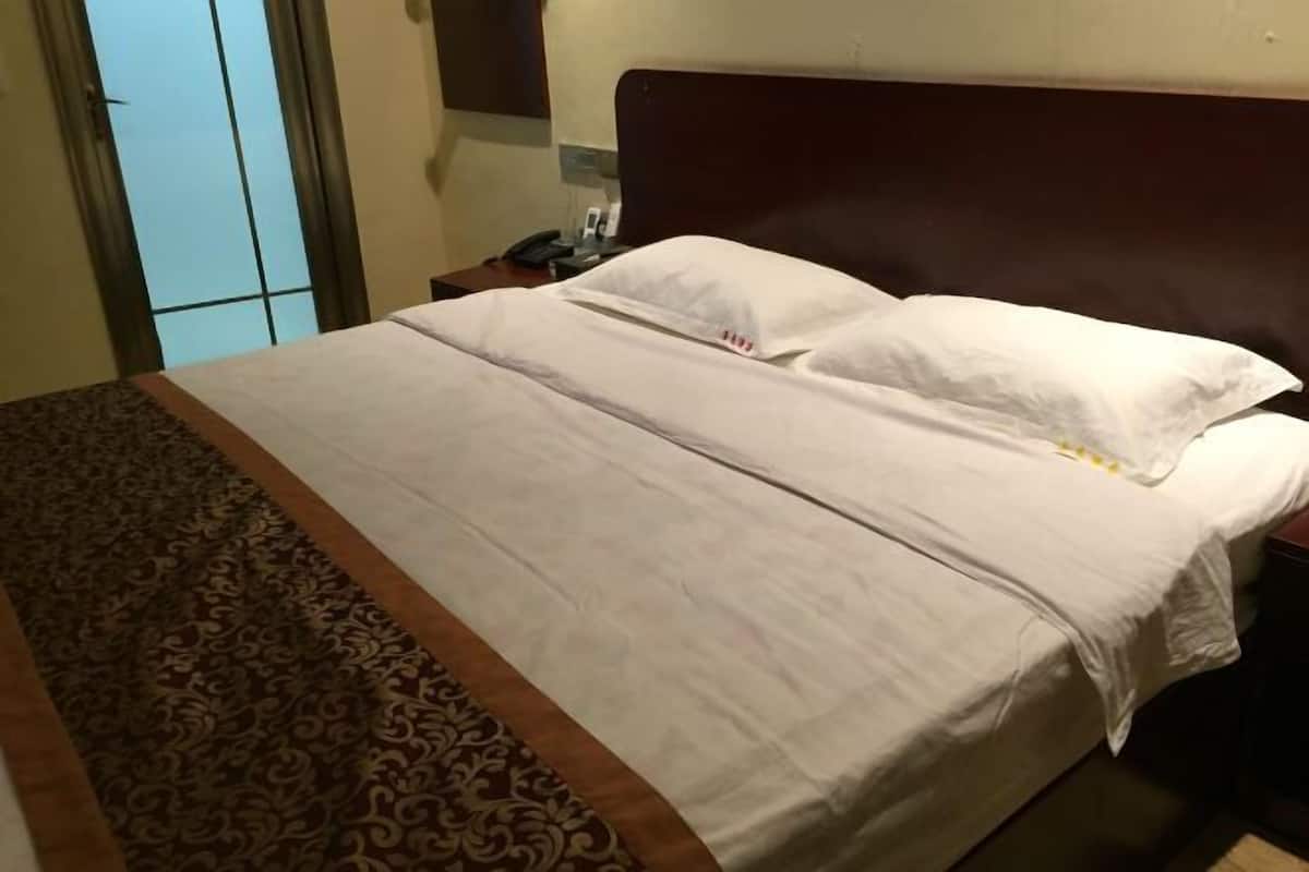 A neatly made bed with white linens and a brown patterned runner.