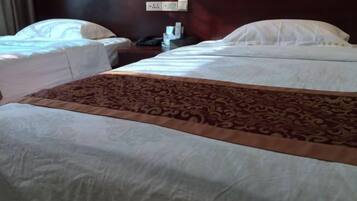 A hotel room with two single beds, a large bed with a patterned bedspread, and a nightstand with a phone and a lamp.