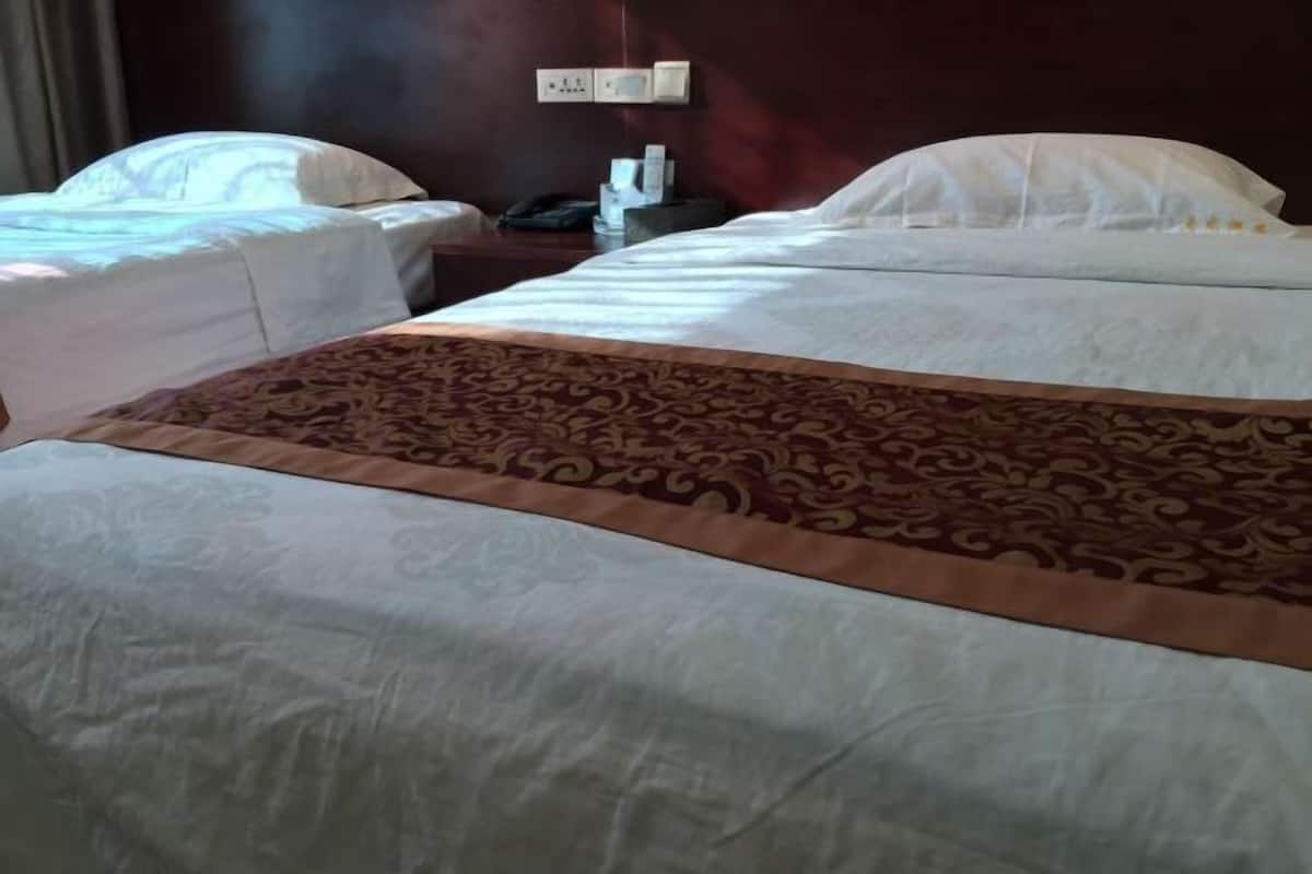 A hotel room with two beds, a patterned bedspread, a nightstand with a phone and a lamp, and a wall socket.