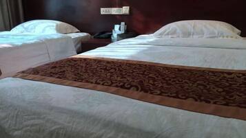 A hotel room with two beds, a patterned bedspread, a nightstand with a phone and a lamp, and a wall socket.
