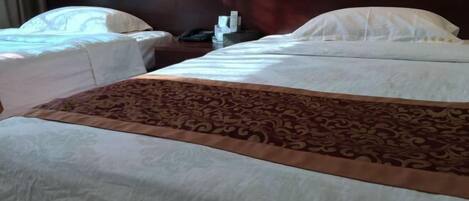 Une chambre d’hôtel avec deux lits, une couvre-lit à motifs, une table de chevet avec un téléphone et une lampe, et une prise électrique au mur.