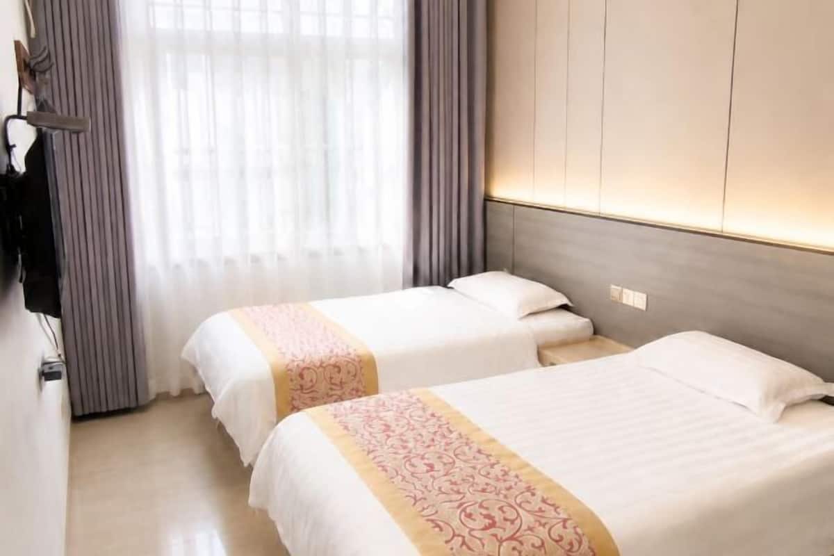 Hotellihuone, jossa on kaksi sänkyä, vaatekaappi ja ikkuna, jossa on verhot.