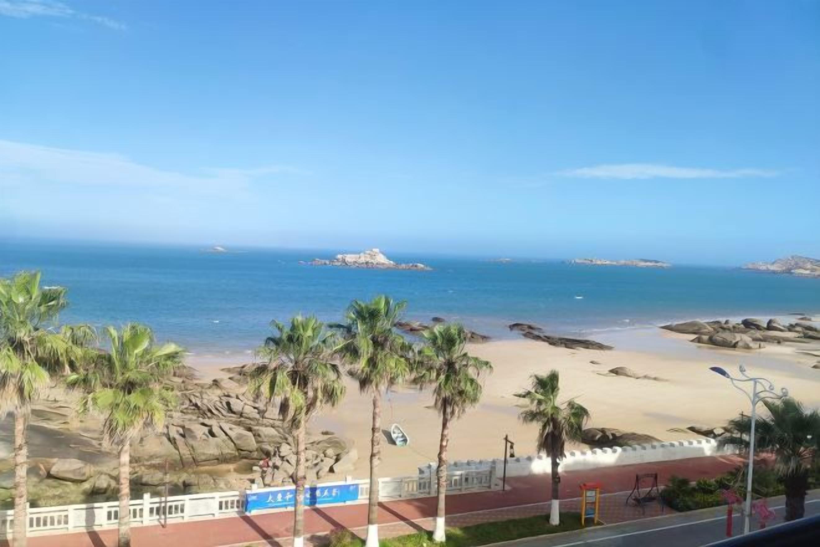 Une plage avec des palmiers, un ciel dégagé et un promontoire rocheux à l’horizon.