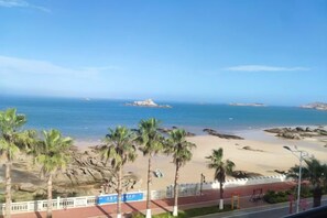 A beach view with palm trees, a clear sky, and a rocky outcrop in the distance. - Yinghaiju Hotel, Weizhou Island (Putian)