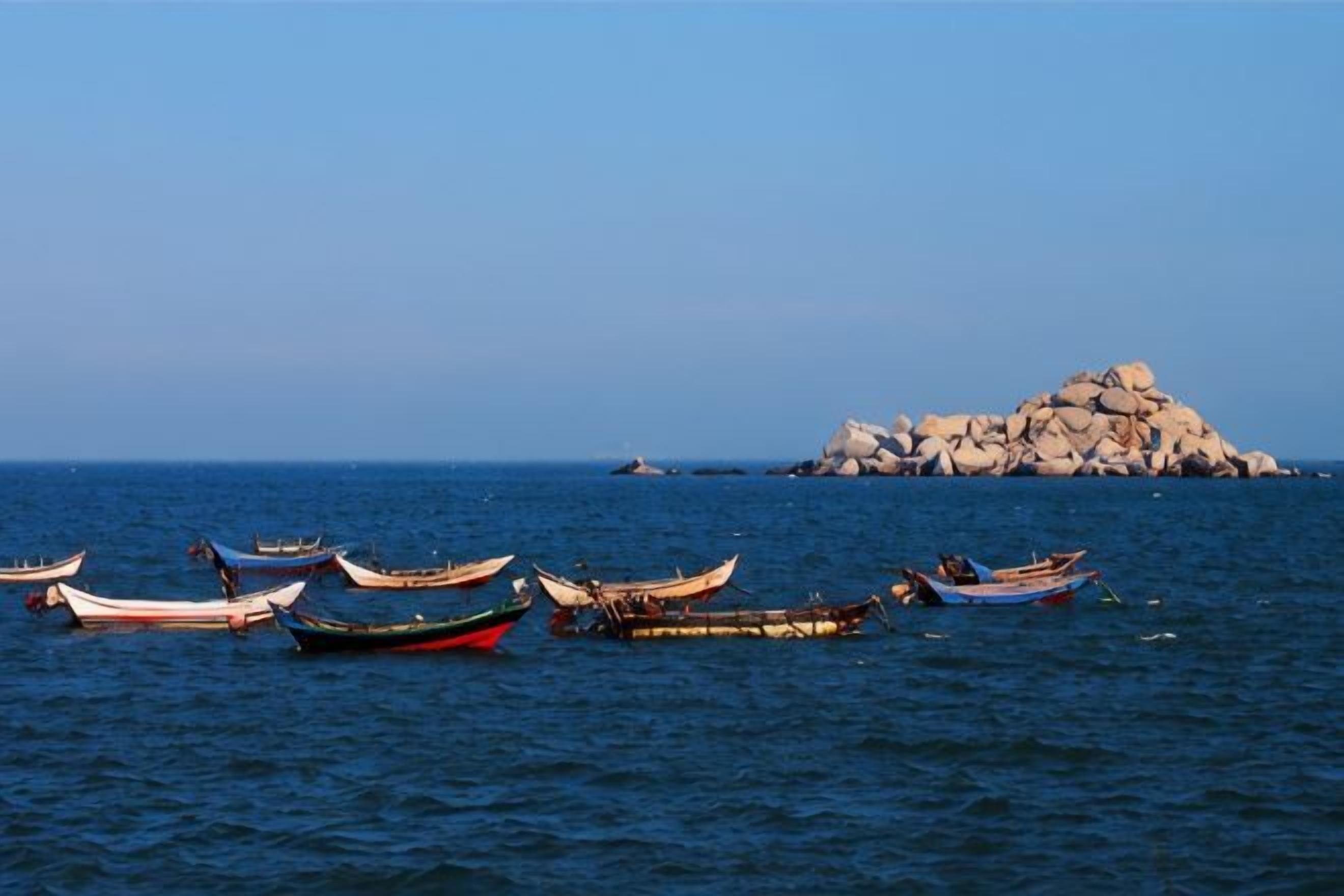 Varias embarcaciones fondeadas cerca de una isla rocosa en el mar.