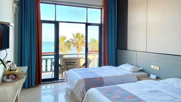 A hotel room with two beds, a balcony with a view of palm trees, and a TV on the left. - Yinghaiju Hotel, Weizhou Island (Putian)