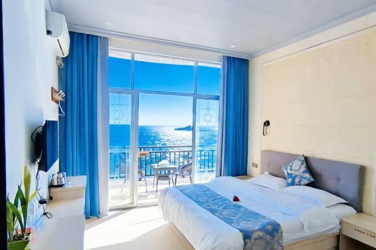 Ein Hotelzimmer mit einem großen Bett, einem Nachttisch, einem Fenster mit Meerblick und einem Balkon mit Tisch und Stühlen.