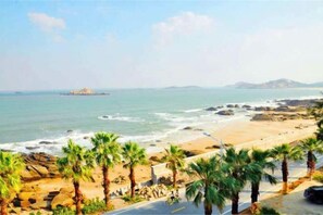 A beach with palm trees, a rocky shoreline, and a distant island. - Yinghaiju Hotel, Weizhou Island (Putian)