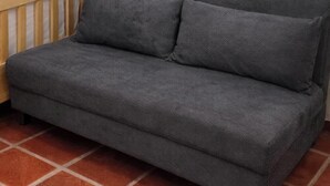 Un canapé gris, recouvert d’un tissu texturé, est placé sur un sol carrelé.